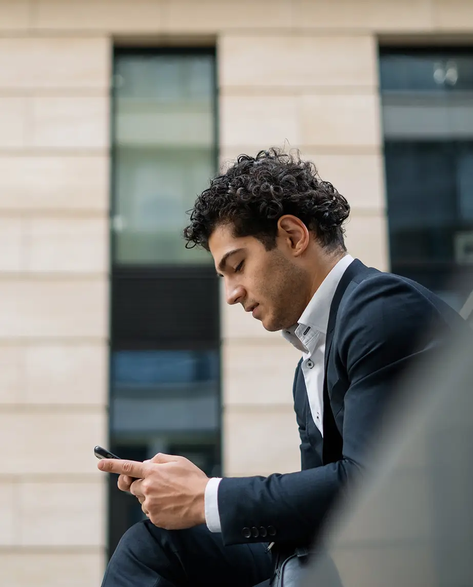 man in a suit, sitting on a bench outside the office, with a phone