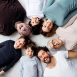 família feliz, com 3 crianças, pai, mãe, avô e avó, deitados cno chão em círculo, vistos de cima