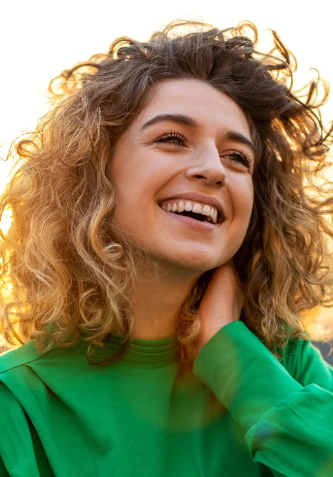 Rapariga com uma camisola verde a sorrir no pôr do sol