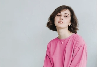 Mulher jovem de cabelo escuro e curto a olhar para a câmara com uma t-shirt rosa