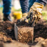 Mãos com luvas a colocar terra num bloco de fundação no solo
