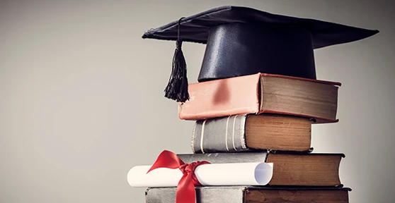 stack of books with a graduation cap (mortarboard) placed on top, and a rolled-up diploma tied with a red ribbon