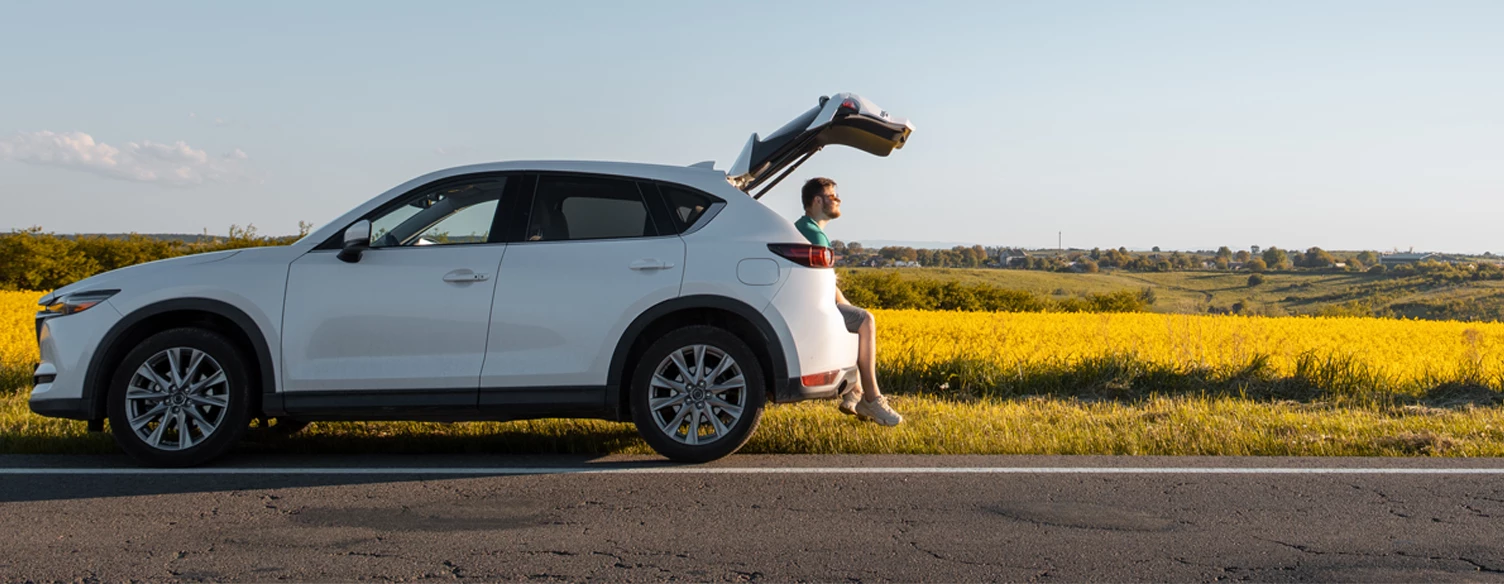 white car parked on the roadside, with the trunk open and a man sitting inside