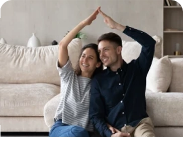 Casal sentado no chão, a sorrir e a fazer forma de casa com os braços
