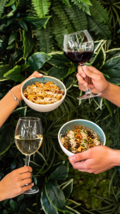 Hands holding glasses of wine and food bowls in a tropical setting