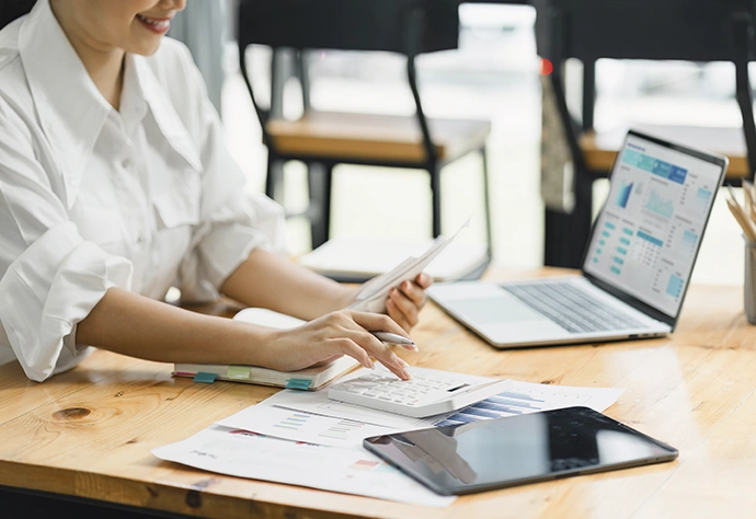Woman smiling while managing finances at a desk with a laptop, calculator, and documents
