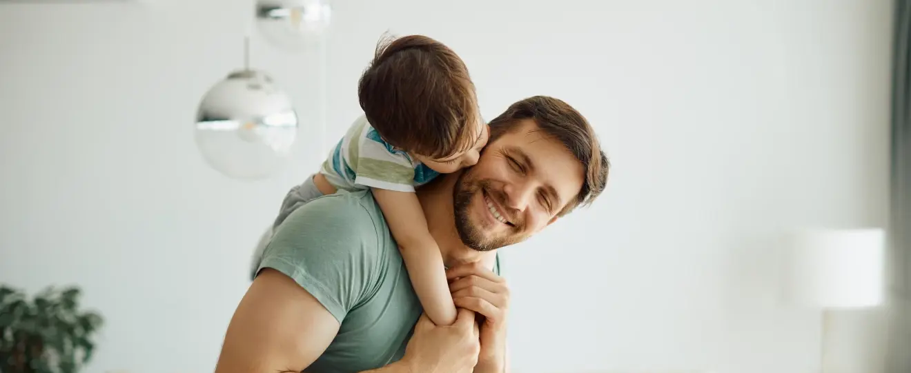 Pai a carregar o filho às costas, filho a beijar-lhe a bochecha