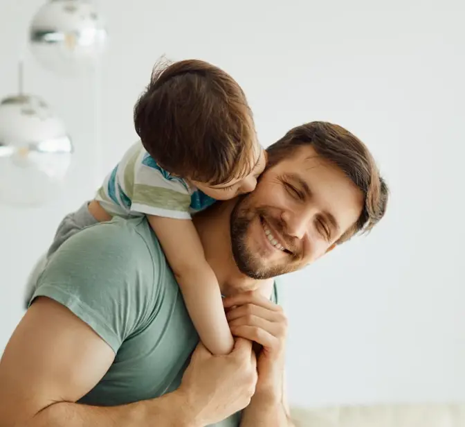 Pai a carregar o filho às costas, filho a beijar-lhe a bochecha