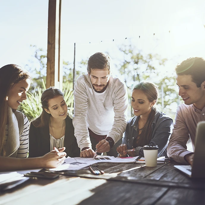 Cinco pessoas em mesa no exterior, onde um rapaz está a mostrar uma folhas de gráficos