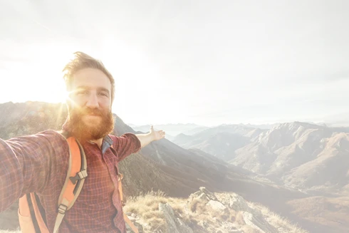homem de barba, no topo de uma montanha, de braços abertos