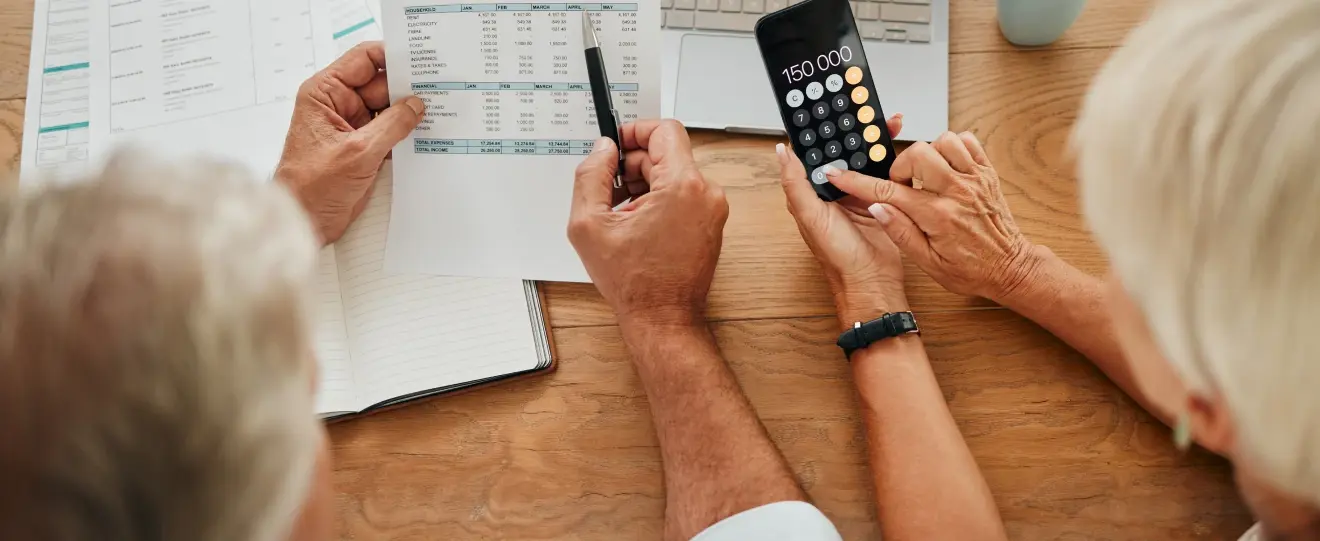 Casal sénior analisa documentos financeiros e usa uma calculadora para planear a reforma