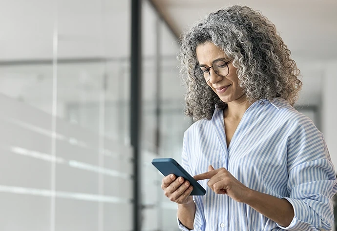 Mulher de cabelo grisalho usa o telemóvel num escritório