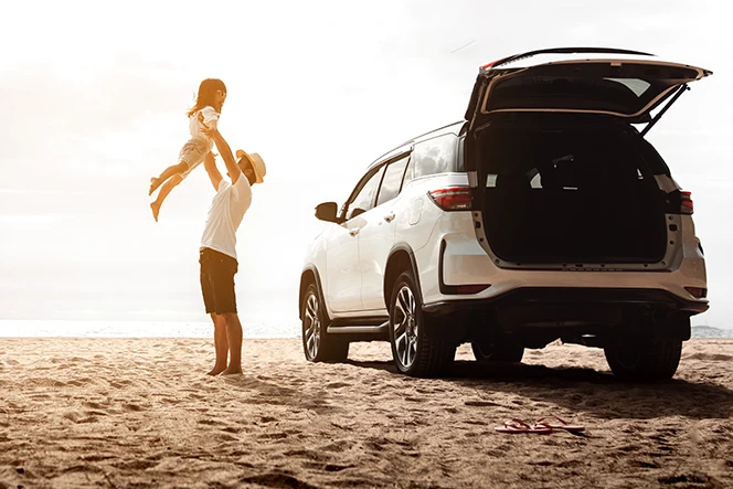 man lifting his daughter in his arms, next to his new car