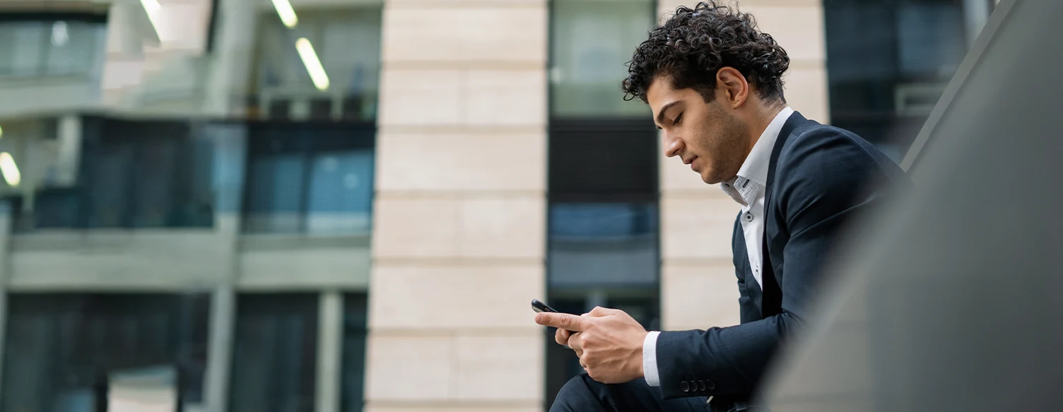 man in a suit, sitting on a bench outside the office, with a phone