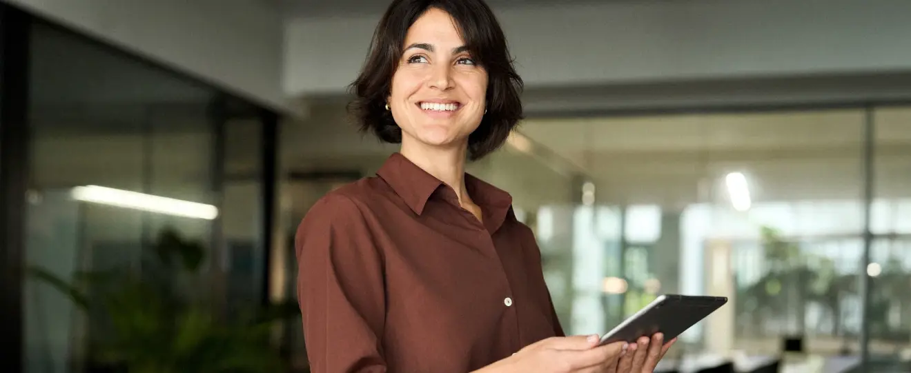 Mulher sorridente com tablet na mão, a olhar para cima num escritório
