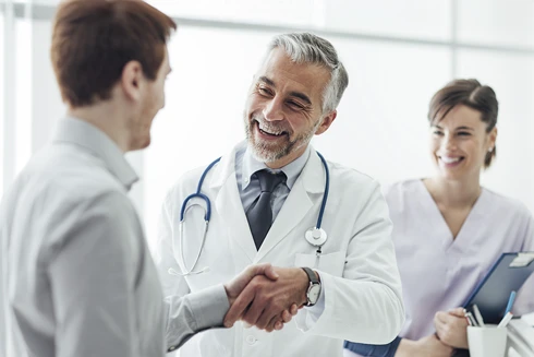 médico com estetoscópio ao pescoço, a dar aperto de mão a paciente