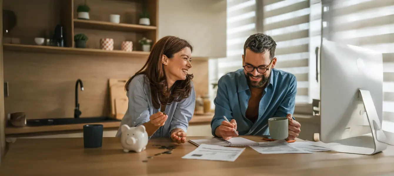 Casal a sorrir na cozinha a analisar documentos e um computador portátil
