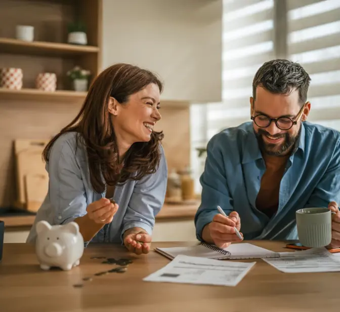 Casal a sorrir na cozinha a analisar documentos e um computador portátil