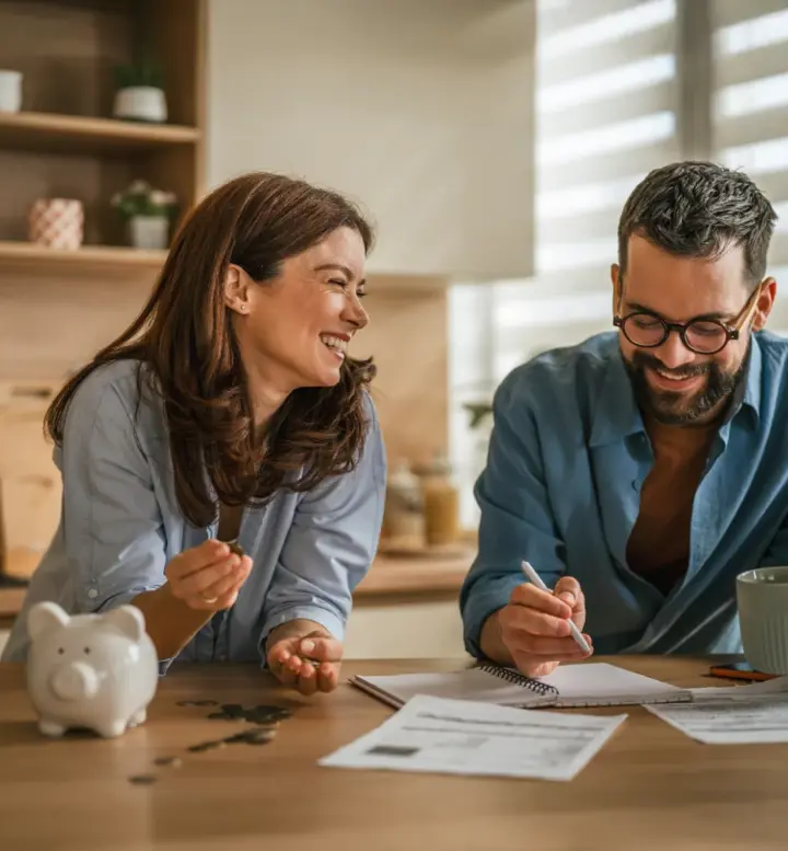 Casal a sorrir na cozinha a analisar documentos e um computador portátil