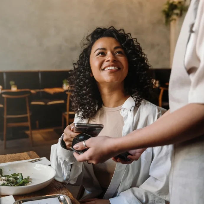 Mulher a sorrir enquanto realiza um pagamento digital com o telemóvel através de tecnologia contactless num restaurante