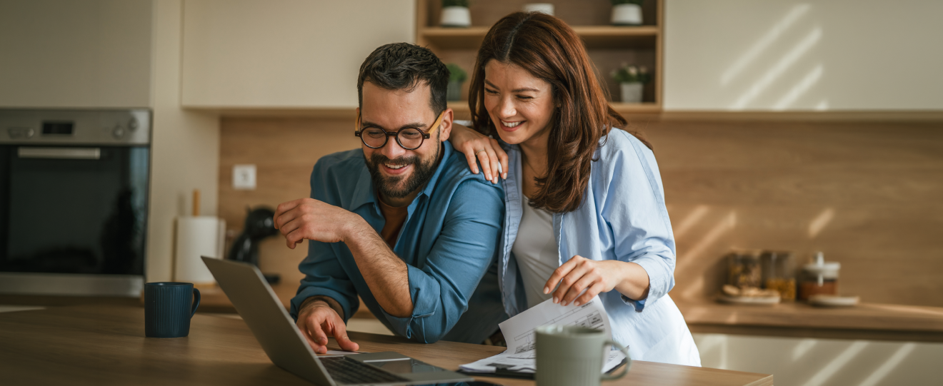 Casal sorridente a usar o portátil na cozinha
