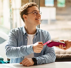 homem sorridente a pagar conta com cartão contactless num TPA
