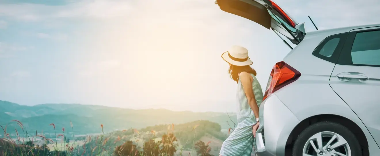 Mulher sentada na bagageira aberta de um carro a observar a paisagem