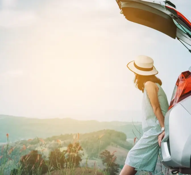 Mulher sentada na bagageira aberta de um carro a observar a paisagem