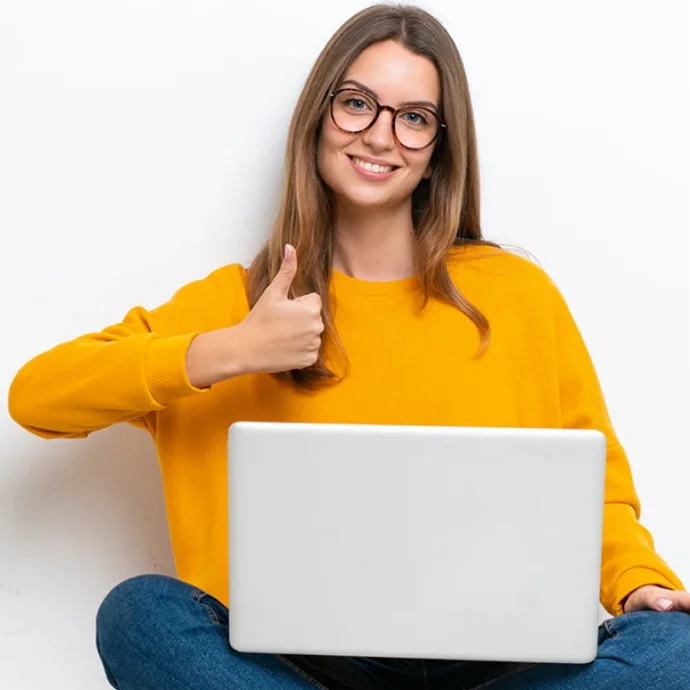 Rapariga sentada no chão com as pernas cruzadas, com um computador no colo e fazer um sinal de fixe 
