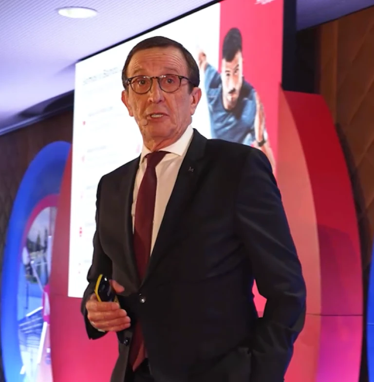 Homem, de óculos, fato e gravata vermelha, a dar uma palestra