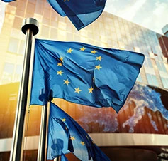 bandeira da União Europeia em frente a edifício espelhado, à luz do nascer do sol