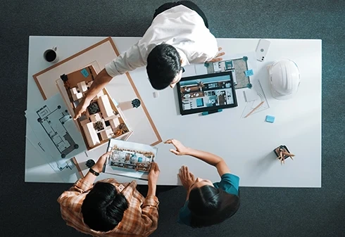 Vista de cima de dois arquitetos a discutir um projeto com plantas e uma maqueta