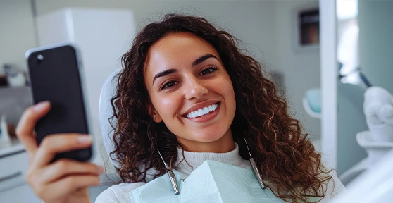senhora sorridente no dentista, a tirar selfie com telemóvel