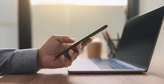 Mão a segurar um telemóvel em frente a um computador portátil