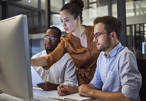Dois homens e uma senhora a analisarem dados no ecrâ de um computador