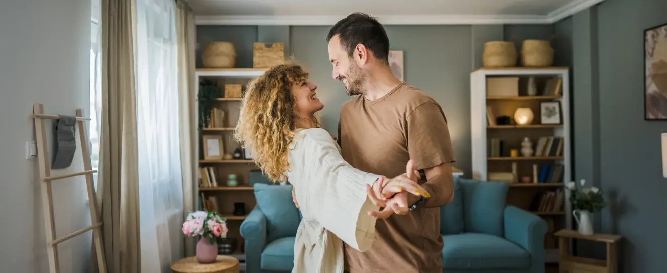 Casal a dançar e a sorrir um para o outro numa sala de estar