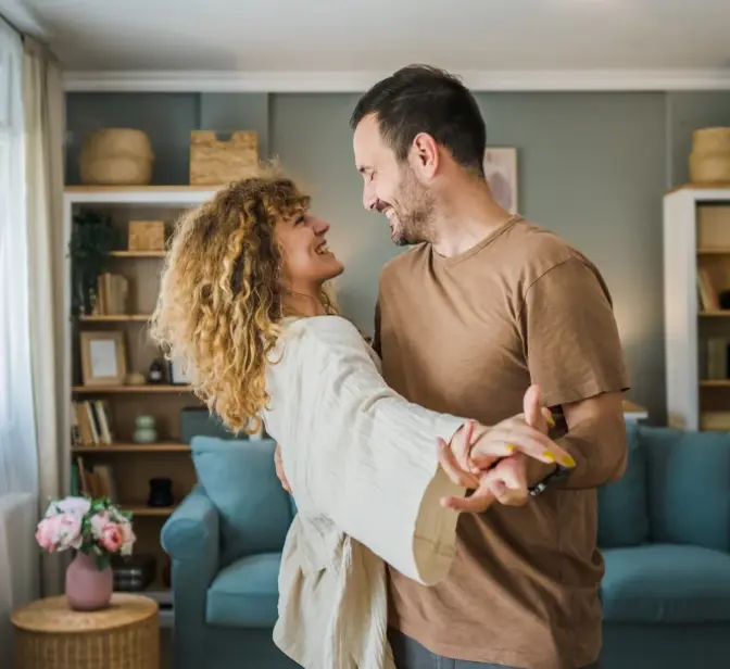 Casal a dançar e a sorrir um para o outro numa sala de estar