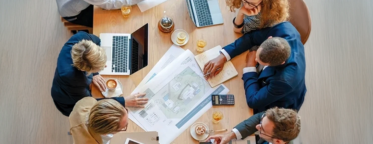Equipa a analisar plantas de arquitetura numa mesa de reunião