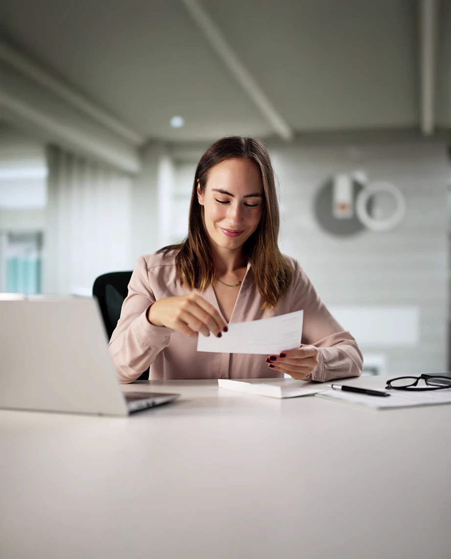 senhora sorridente num escritório, com carta cheque na mão