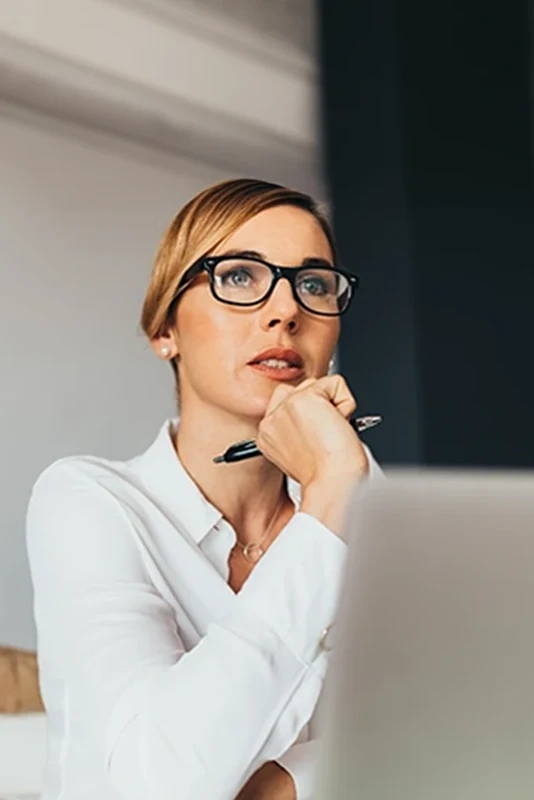 Senhora em frente a computador, com caneta na mão
