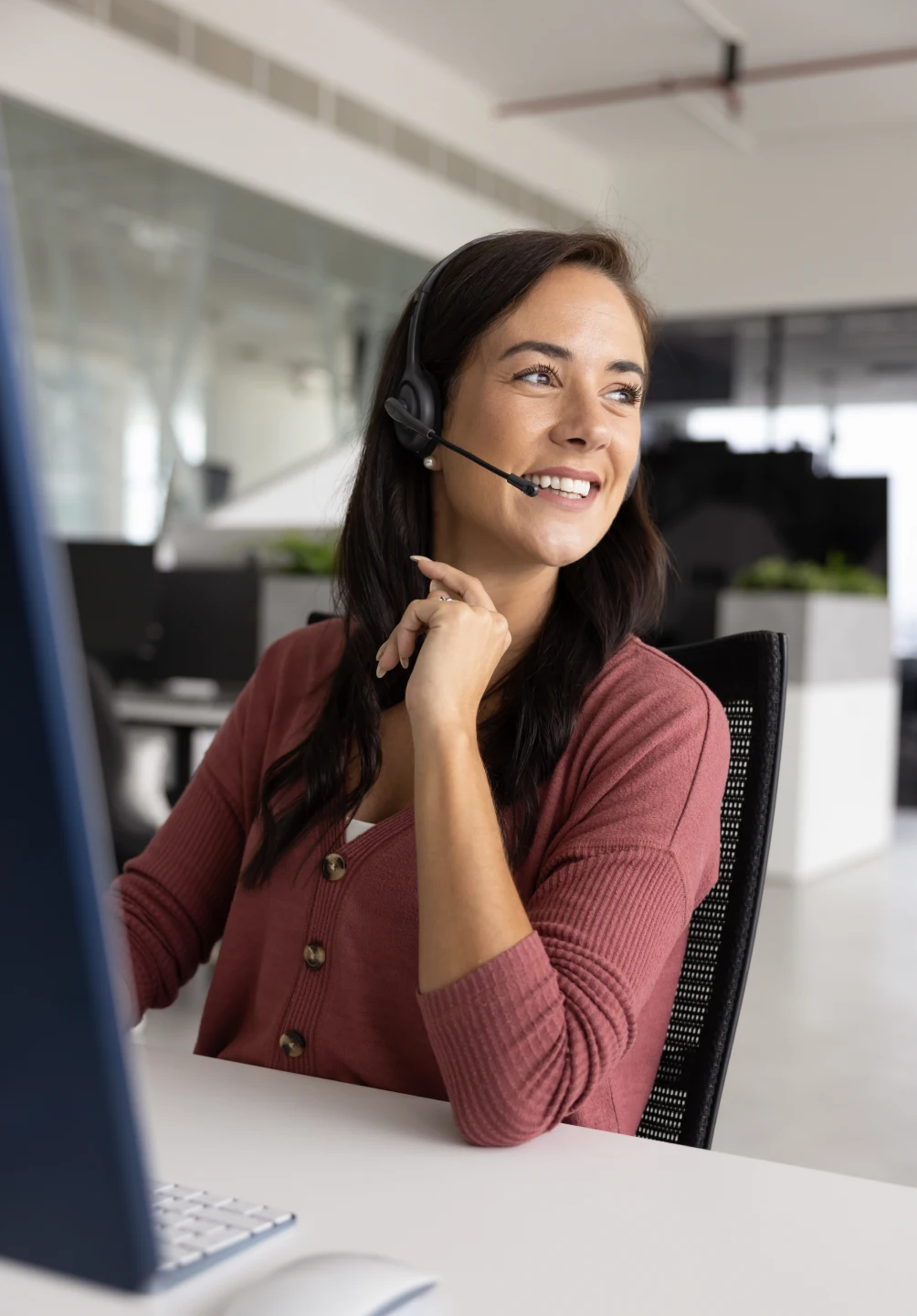 senhora sorridente num centro de contactos, com headset e computador
