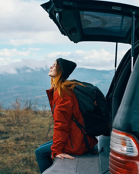 woman sitting in the open trunk of a car, on a landscape of mountains