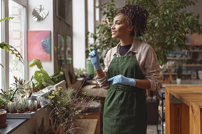 senhora com avental verde e luvas, num viveiro de platas