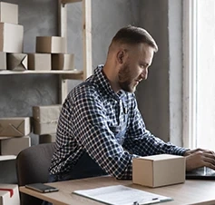Man working on a laptop in an office with parcel boxes