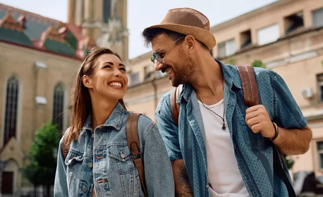 Casal sorridente com mochilas a passear numa cidade histórica