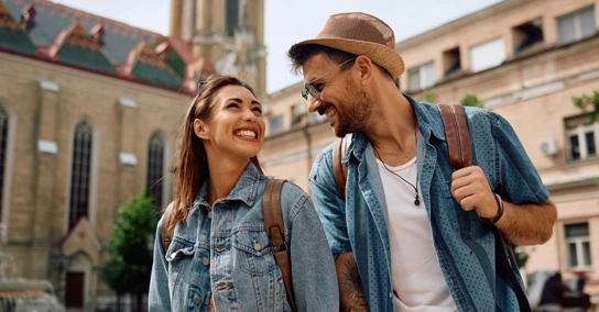 Casal sorridente com mochilas a passear numa cidade histórica