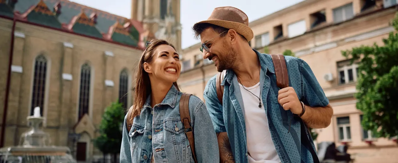 Casal sorridente com mochilas a passear numa cidade histórica