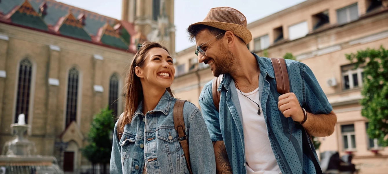 Casal sorridente com mochilas a passear numa cidade histórica