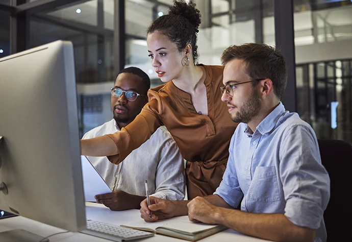 Dois homens e uma senhora a analisarem dados no ecrâ de um computador