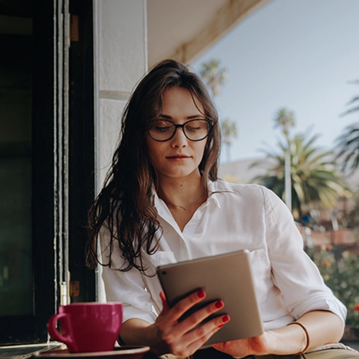 Woman using a tablet on a terrace with a coffee cup